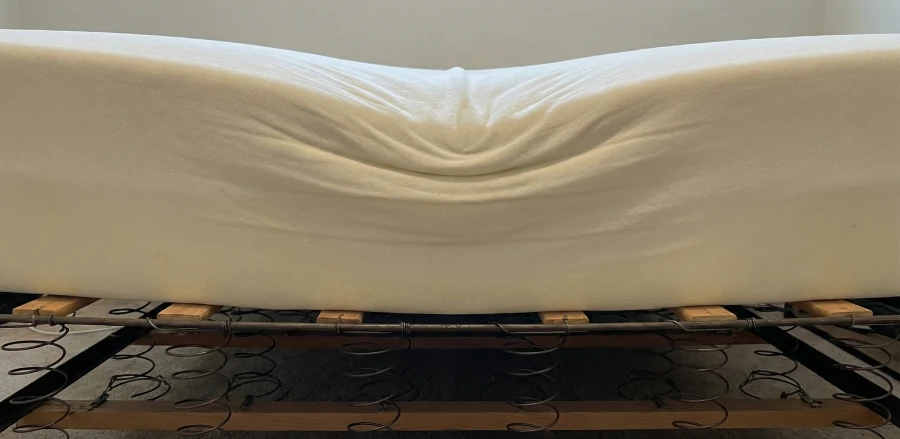 A memory foam mattress sagging significantly in the middle while resting on an old-fashioned wire and wood box spring.
