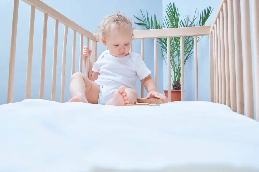 A toddler sitting up and playing on a dual-sided crib mattress, showing the durability and support needed for growing children.