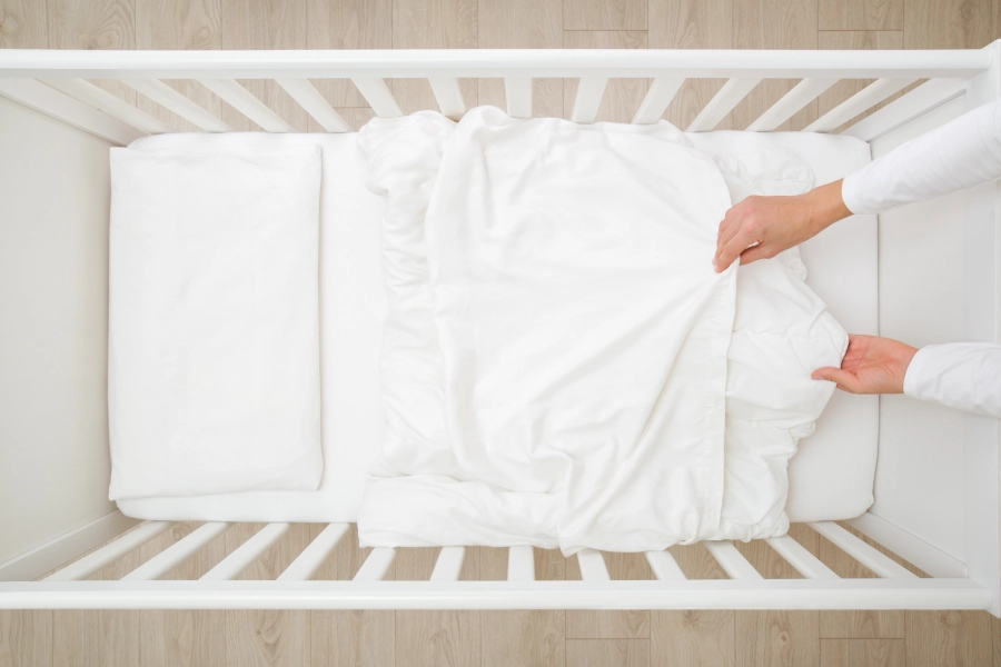 Overhead view of a parent fitting a sheet onto a standard crib mattress to demonstrate a snug, gap-free fit for safety.