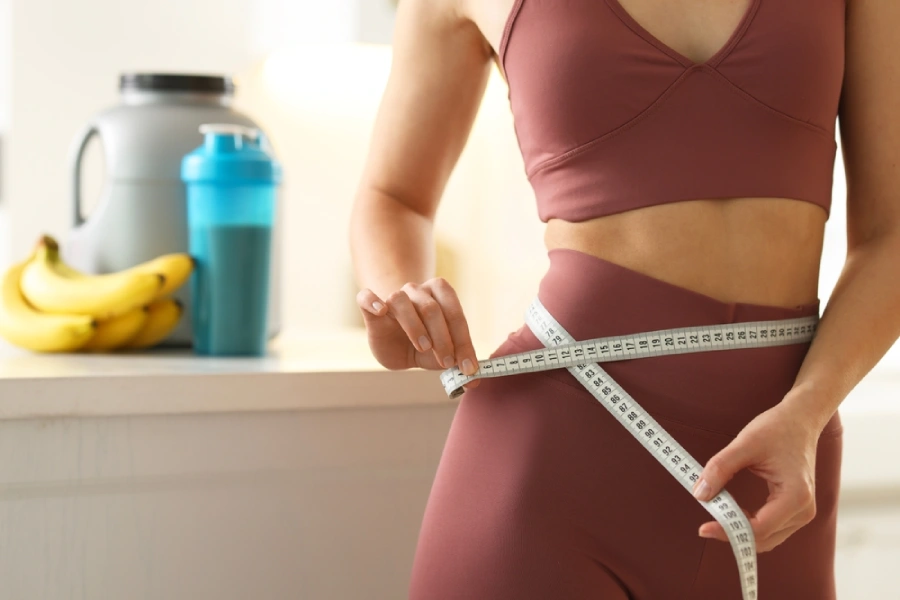woman in activewear using measuring tape to measure weight loss