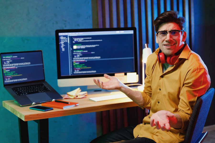 Man shrugging with code open on his computer monitor