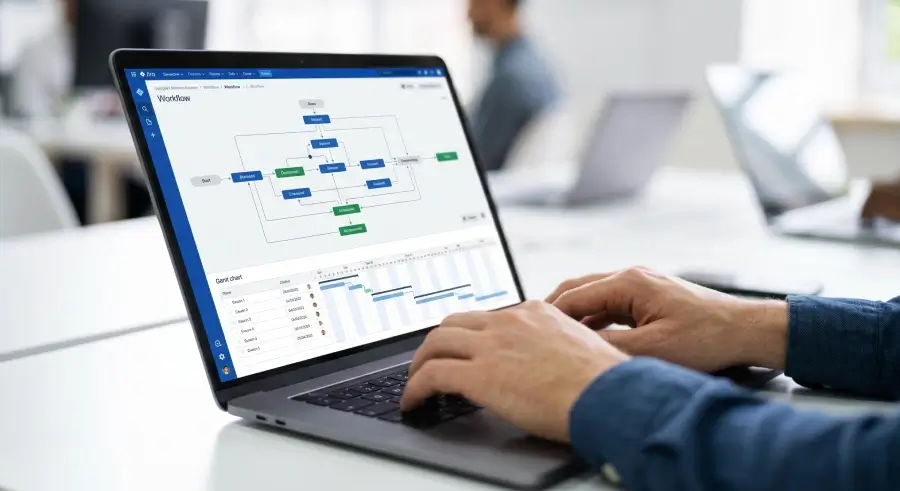 Close-up shot of a developer's hands typing on a laptop, with the screen displaying a complex visual workflow and Gantt chart visualization.